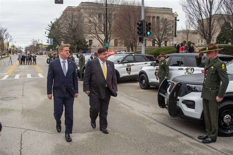 Gov. JB Pritzker and Illinois State Police Director Brendan Kelly walk alongside a fleet of new squad cars and rank-and-file Illinois State Police troopers outside the Illinois State Capitol Tuesday. They were commemorating ISP's 100th anniversary.