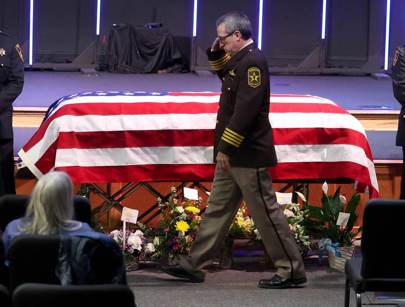 Law enforcement officers salute as they pass by the casket of former DeKalb County Sheriff Roger Scott during a law enforcement walk-through at the visitation for Scott Thursday, March 6, 2025, at Bethany Road Bible Church in DeKalb. Scott, who was the county sheriff for more than 30 years, died on February 23 at the age of 78.