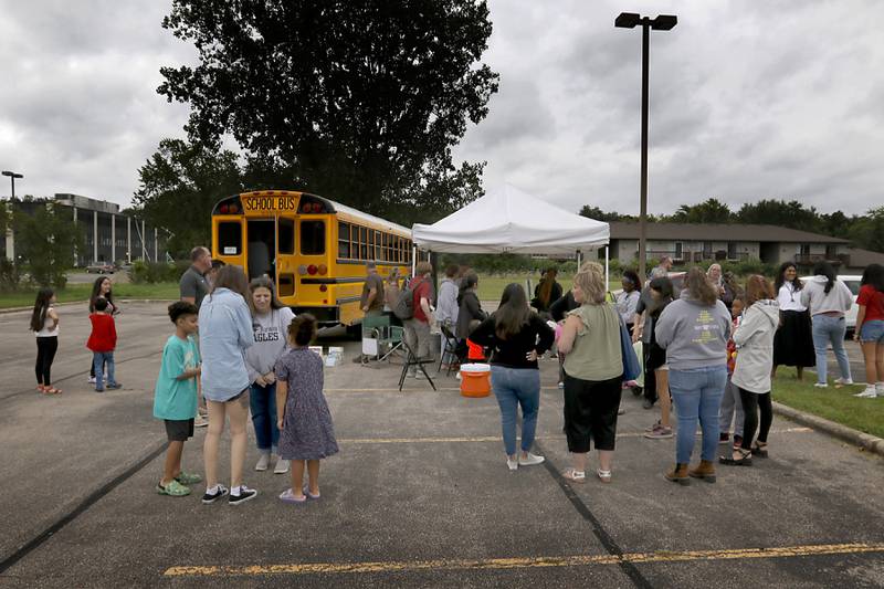People gather around a school bus during a Woodstock School District 200 Back to School Coming to You event at Sheila Street Apartments on Tuesday, Aug. 6, 2024. The location was one of twelve stops on the tour that gave out backpacks and school supplies, provided registration help and computer repair.