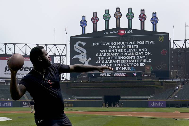 Cleveland Guardians outfielder Franmil Reyes throws a football to teammate Myles Straw as the scoreboard informs fans that Wednesday's game between the Chicago White Sox and the Guardians has been postponed due to multiple positive COVID-19 tests within the Guardians organization.