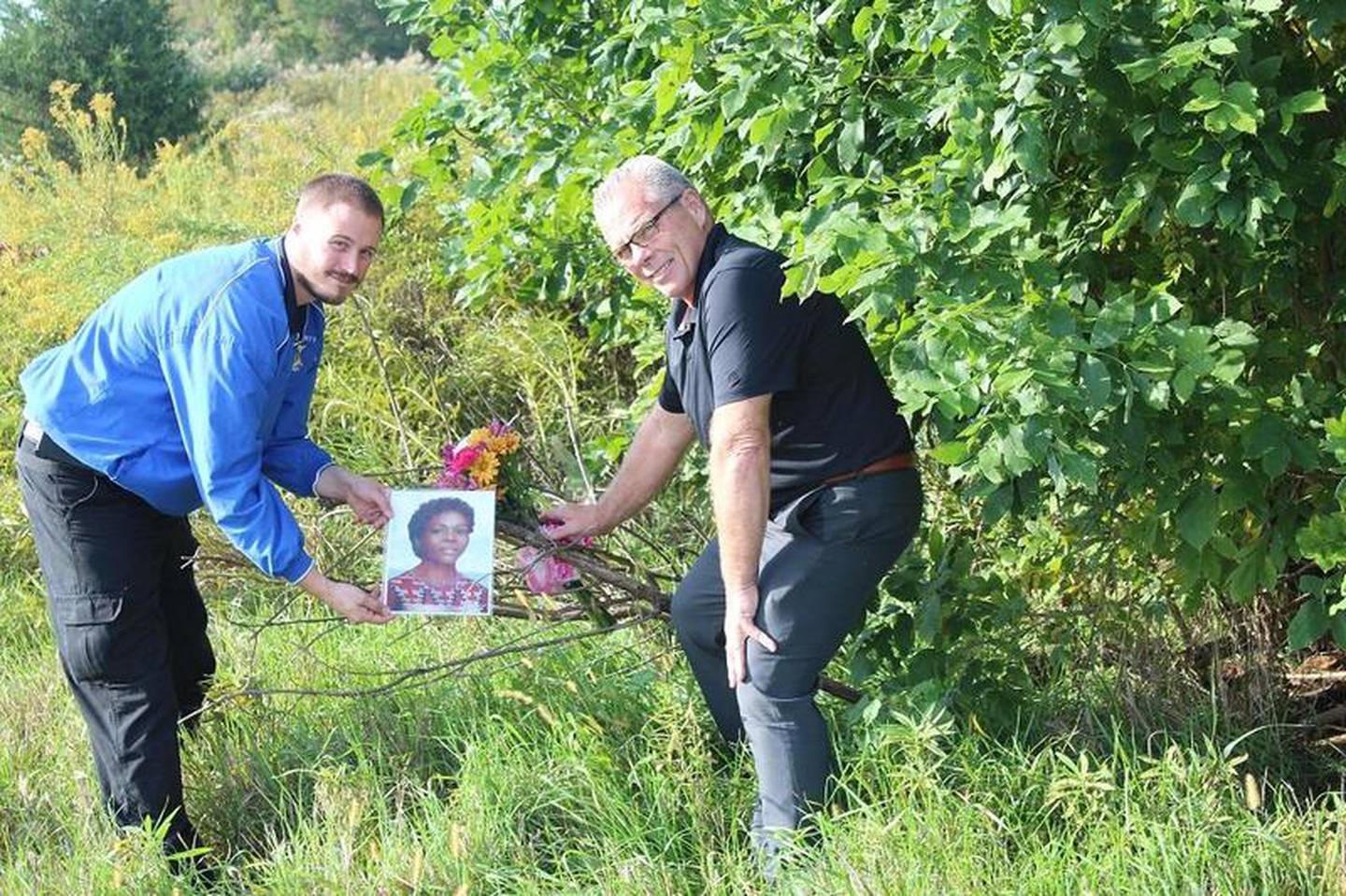 Grundy County Deputy Chief Coroner Brandon Johnson (left) and Coroner John W. Callahan  placed flowers and an artist-rendered-image of a 1976 murder victim on Monday near the site of her discovery 43 years ago.