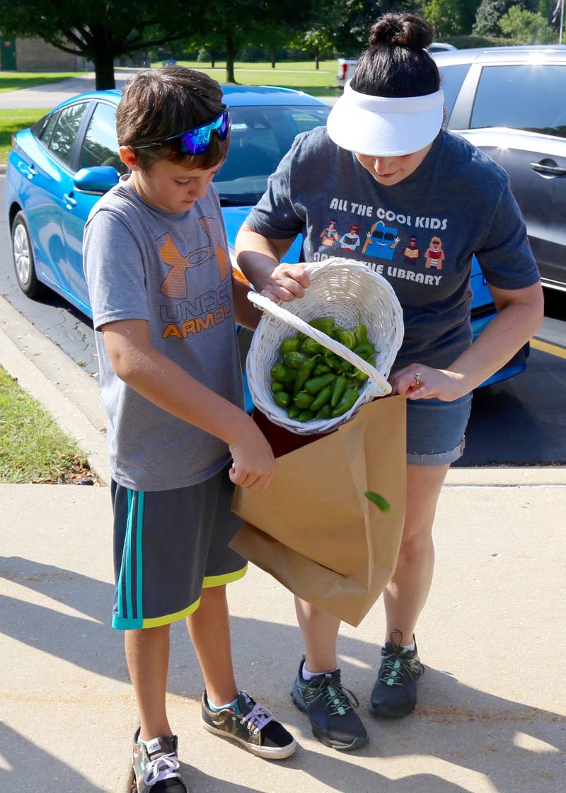 Jayden Devine helps Youth Services Manager of the Town and Country Library, Gina Knowlton, pour freshly picked peppers into a bag in Elburn on Saturday, Sept. 3, 2022.