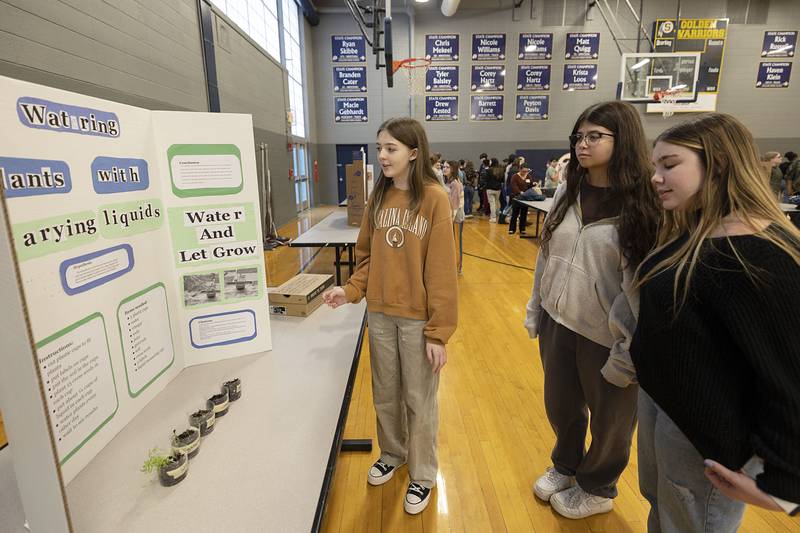 Cora Enright (left) discusses her exhibit on watering plants with varying liquids with fellow students Izzy Fagerman and Juliet Funderberg during a STEM exhibit at Challand Middle School Thursday, March 9, 2023.