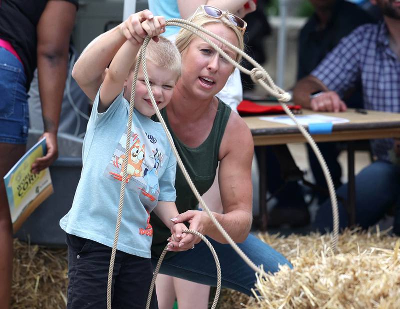 Bently Franklin, 5, from DeKalb, gets some instruction from Danielle Willrett, from the DeKalb-Kane Cattlemen’s Association, on how to lasso a bull Friday, Aug. 22, 2025, during the first day of Corn Fest in downtown DeKalb.