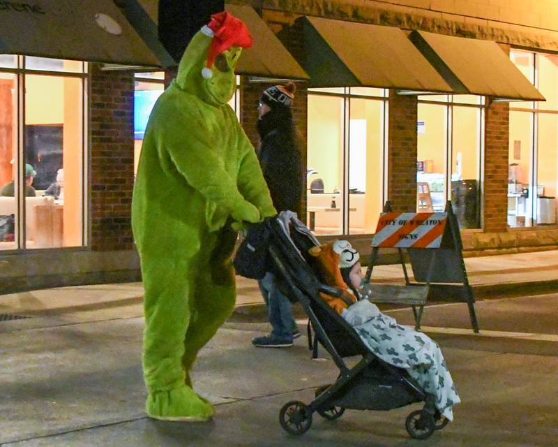 David Mordis of Wheaton dresses up as the Grinch and pushes his Son Jaxon Wolf Mordis, 1 year old, to find a spot along the Wheaton Holiday Parade route downtown Wheaton on Friday Nov. 24, 2023.