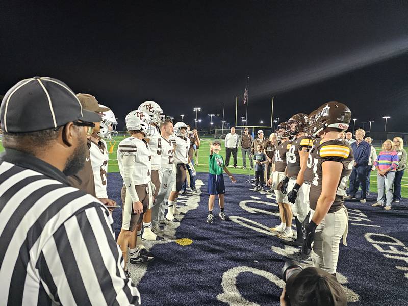 Anthony Hansen, nephew and godson of the late Kevin Hansen, a former Joliet Catholic football player and Mt. Carmel teacher, flips a coin for the game-opening coin toss as captains for the teams and officials look on Saturday, Oct. 11, 2025, in Joliet.