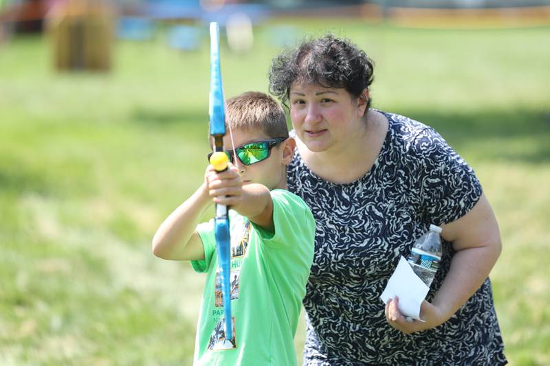 Zlatka Stonanova helps her nephew, Aidan Schwarz aim at a bow target at the Royal Faire hosted by the Joliet Public Library Black Road Branch on Saturday, July 22nd, 2023.