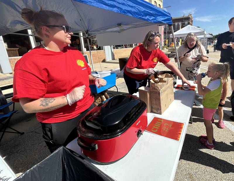 Nicole Gilbert serves a cup of chili to Freya Doeden, 5,  of Polo as her chili-partner Marissa Richardson (left) watches at the annual chili cook off on Saturday, Sept. 27, 2025. Gilbert and Richardson were representing the Polo Shell station team.