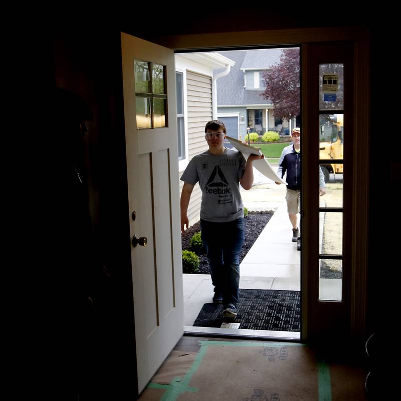 Junior Aaron Hugger and teacher  Erich Parpart carry a stair skirt board into the home that students in the Woodstock Building Trades Program are building in Woodstock on Monday, May 8, 2023. This will be the program’s 43rd completed home since it began in 1972.