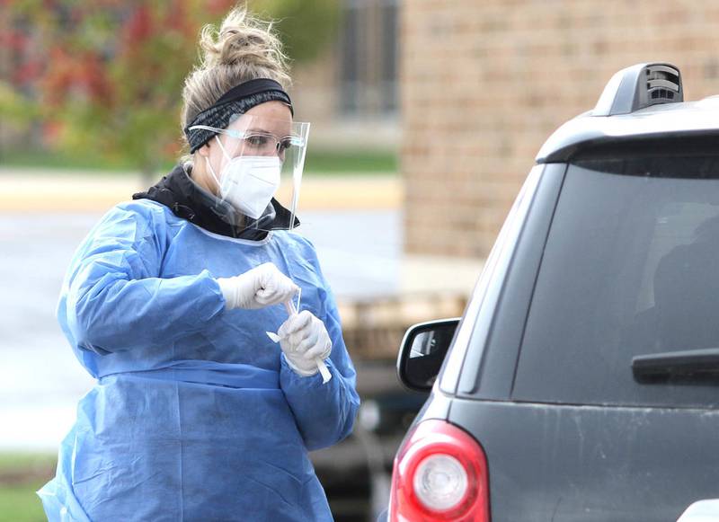 Meghan O'Rorke, a phlebotomist with HR Support, hands out a COVID-19 test at the free drive-thru testing site Oct. 13 at DeKalb High School.