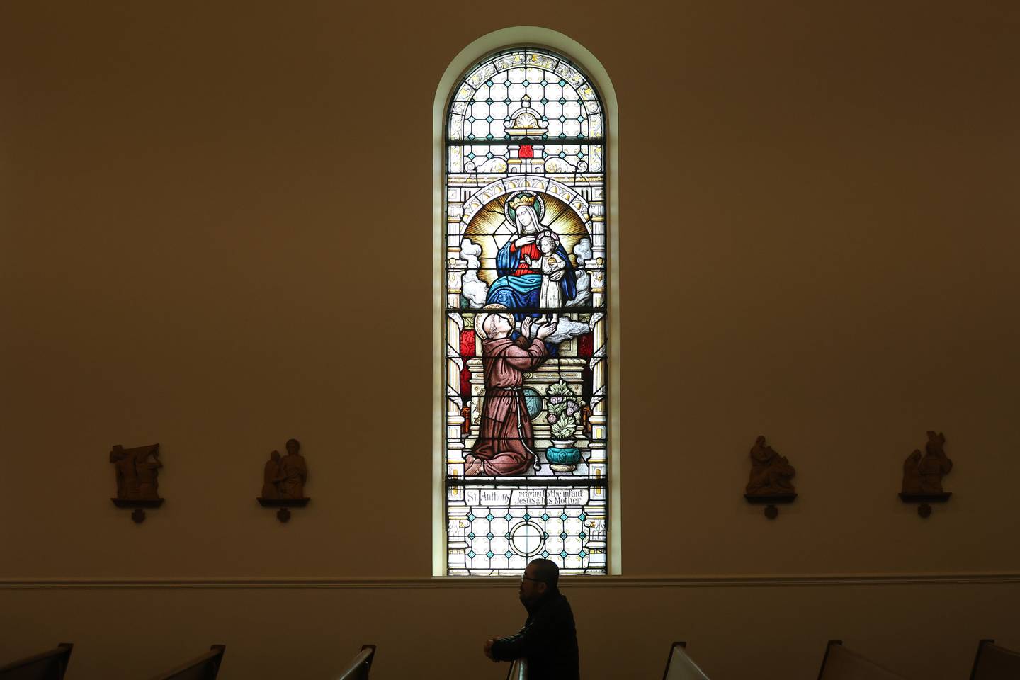 A parishioner prays under a stained glass window depicting St. Anothy praying to Jesus and his mother at Church of St. Anthony on Friday, March 29, 2024 in Joliet.