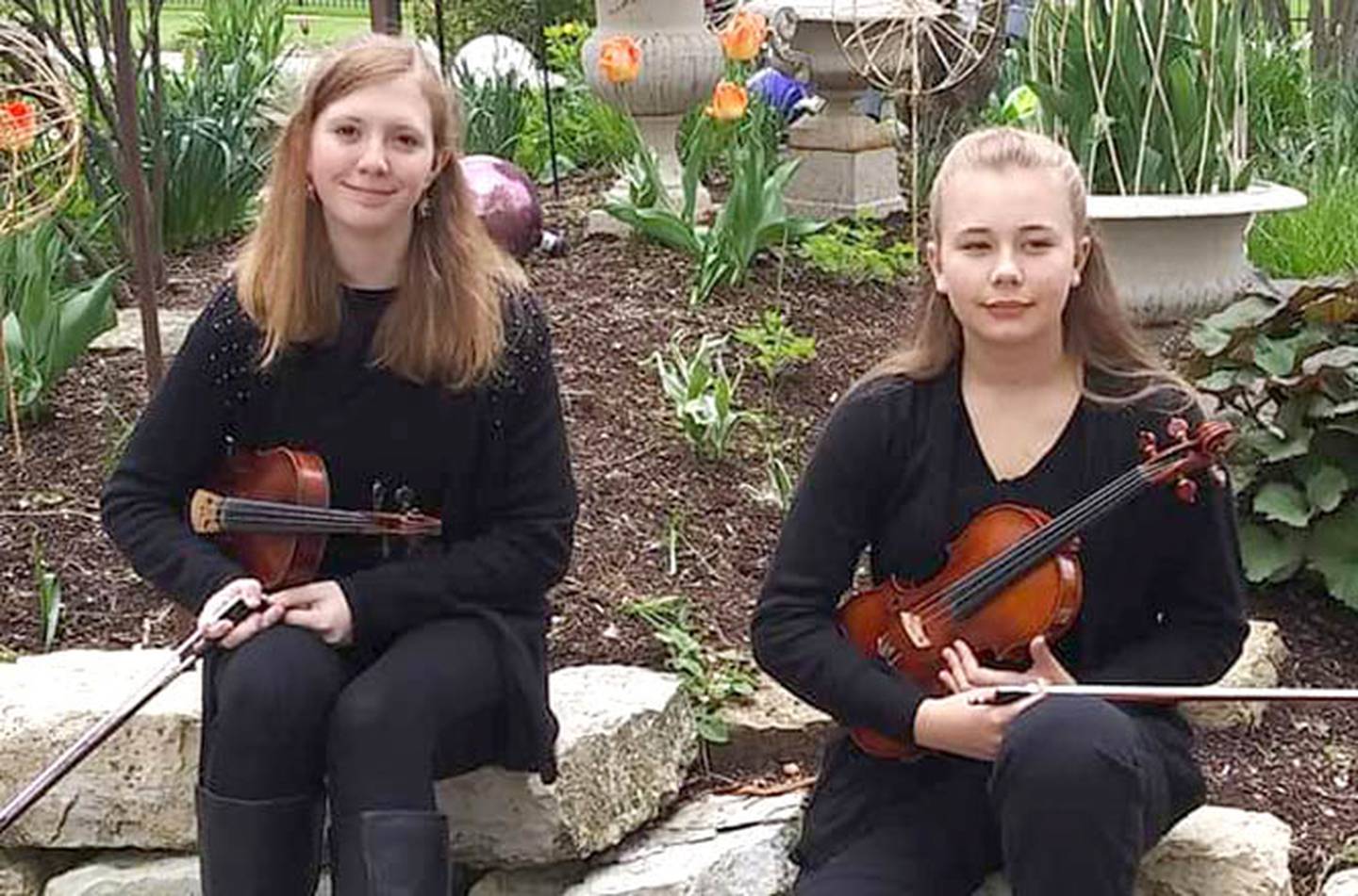 Eva Peterson and Emma Fredericks sit together in a garden with their violins in a photo taken by Fredericks' mom, Eileen Garvin.