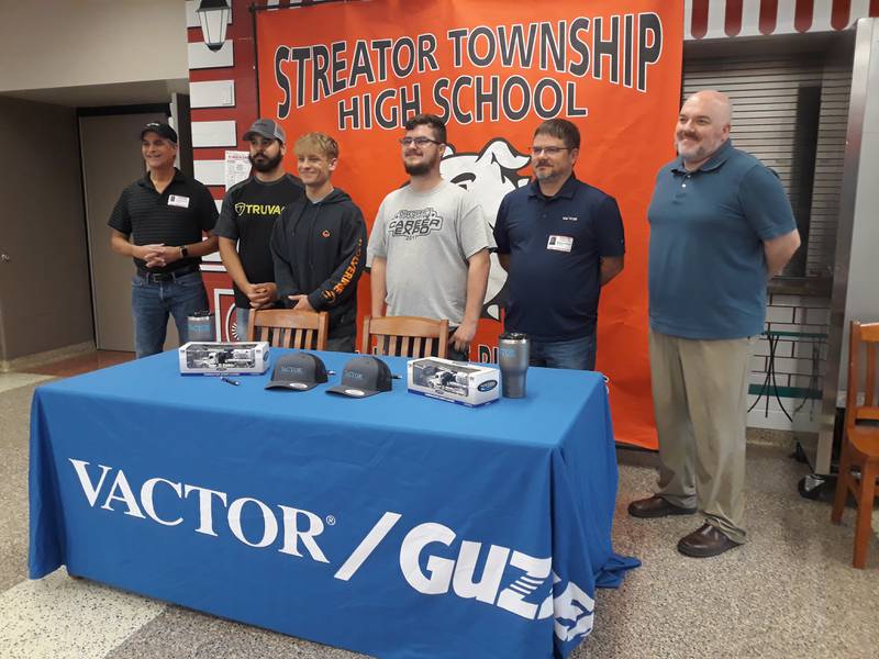 After signing letters of intent Tuesday, May 17, 2022, to work for Vactor Manufacturing, Keegan Emm (third from left) and Carson Trainor (fourth from left) pose for a photo with (left to right) Tim Hackathorn, paint supervisor at Vactor; Shayne Schuler, welding supervisor at Vactor; Matt Bouley, production manager at Vactor; and Chris Peterson, work program coordinator at Streator High School.