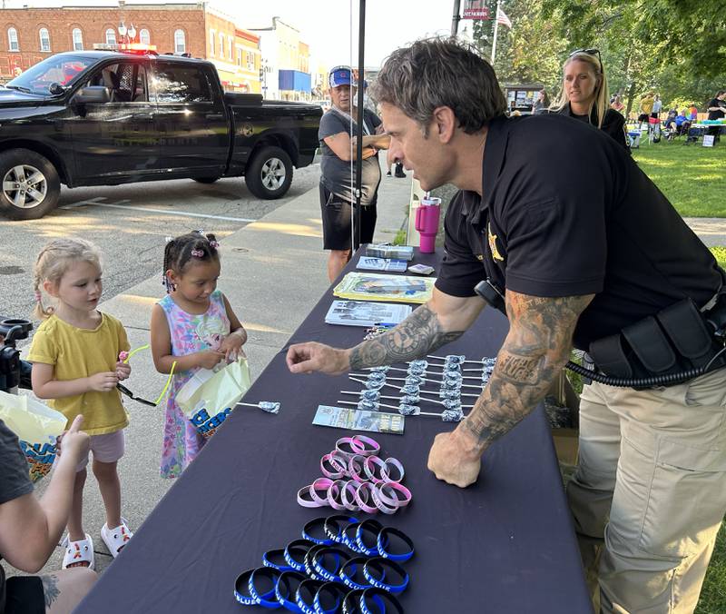 Zuraya Ritt, 4, and Charlette Bostic, 3, pick up some Mt. Morris Police Department accessories from Police Chief Michael Cicchetti at the National Night Out event in Mt. Morris on Tuesday, Aug. 5, 2025. The Mt. Morris Fire Protection District and other agencies also had booths at the evening event.