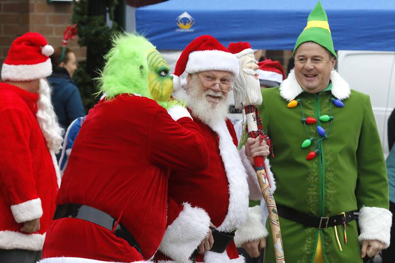 Russ Hyatt of Sundowner Entertainment, dressed as the Grinch, Santa Claus, and  Chris Christensen, dressed as Buddy the Elf, joke around before the start of the McHenry County Santa Run For Kids on Sunday morning, Dec. 3, 2023, in Downtown Crystal Lake. The annual event raises money for agencies in our county who work with children in need.