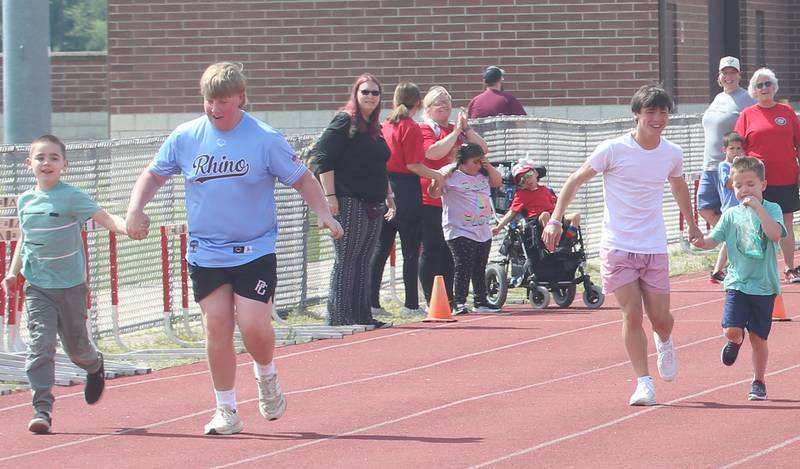 Lighted Way students Layne Gunier, and Alexander Coomer run down the track with the help of Trinity Catholic Academy eighth grade students Maks Bake and Luca Verucchi, during the Lighted Way and Trinity Catholic Academy PALS Spring Track Meet on Monday, May 13, 2024 at the L-P Athletic Complex in La Salle. Lighted way students participated in running, throwing, wheelchair slalom and much more.