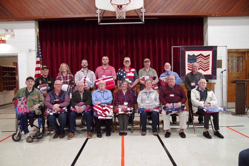 (Front from left) Mike Dunlap, Mike Blakemore, Dave Smith, Ron Austin, Charlotte Seeger, Pat Petersen, Mike McCauley, Ken Morlan, (back, from left) Larry McCann, Jen McMullen, Colin Betken, Jim Meiners, Dan Petersen, Rick Topolski, Tom Hallam and Robert Danko receive Quilts of Valor on Sunday, Nov. 12, 2023, at Holy Trinity Church Fellowship in Streator.