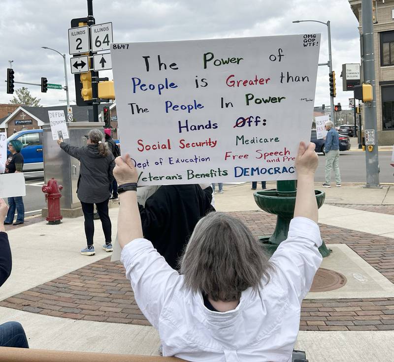 One of  the approximately 250 people who attended a Hands Off rally on Saturday, April 19, 2025 in Oregon, holds a sign as cars pass through the intersection of state routes 64 and 2. Participants carried signs critical of  the Trump administration.