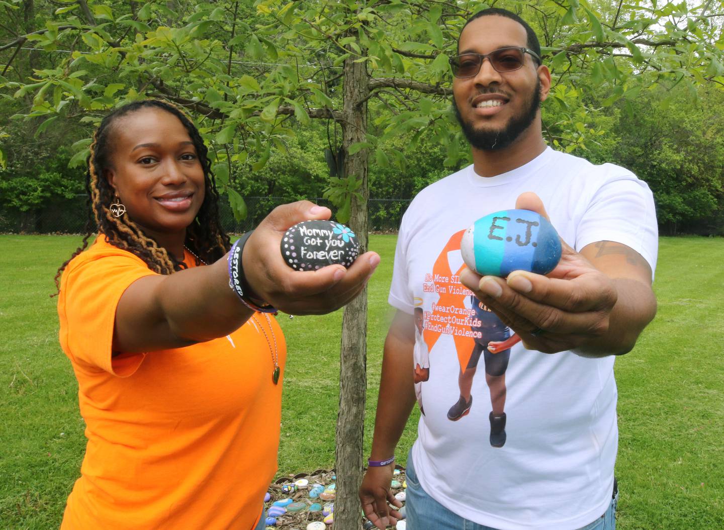 Andrea Elion, mother of Ezra Hill Jr., and Brandon Elion, Ezra’s stepfather, hold painted rocks Monday, May 12, 2025, near the tree and rock garden dedicated to Ezra's memory at Tyler Elementary School in DeKalb. Ezra was shot and killed in 2019 in Harvey. The Ezra Hill Jr. Memorial Rock Painting event will be held June 7 at the school in DeKalb.
