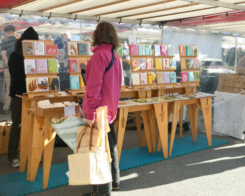 Stacy Jacobs of Hinsdale buys cards from Silkscreen cards during the Wheaton French Market in downtown Wheaton on Saturday April 13, 2024.