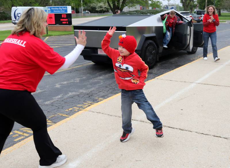 Marshall Morong, 7, a first grader at Hinckley-Big Rock Elementary School, high-fives his teacher Mindy Spinney as his mom Jessica Satdei and sister Carolynn Morong, a fourth grader at the school, exit their ride Monday, May 5, 2025, as he arrives for his first day back at school after missing months waiting for, and eventually receiving, a heart transplant. Morong arrived in style in a Tesla Cybertruck donated for use by Telsa of Naperville, along with an escort by Hinckley and Big Rock first responders.