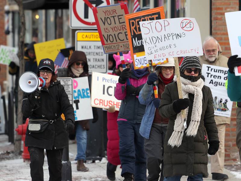 Protesters chant and carry signs as they march west down the sidewalk on Lincoln Highway in DeKalb Tuesday, Jan. 20, 2026, as part of a larger national Free America Walkout. The group is protesting what they perceive as an escalating fascist threat under President Donald Trump and his administration.