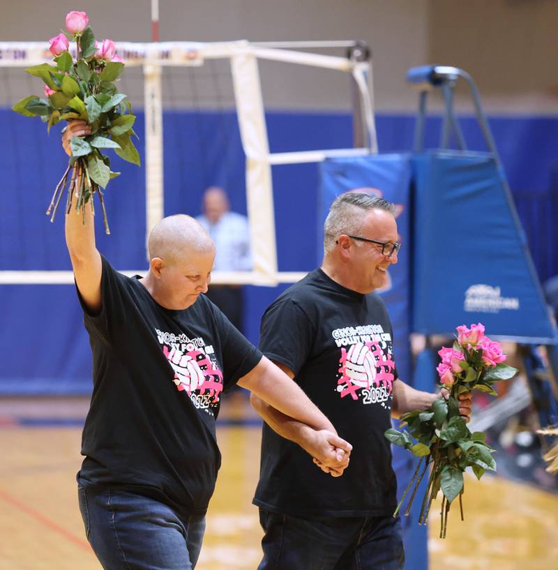 Becky Cleveland salutes the crowd as she is escorted off the court by her husband David after being recognized as the guests of honor before the Genoa- Kingston volleyball team's Volley for the Cure breast cancer fundraiser match against Oregon Wednesday, Sept. 21, 2022, at Genoa-Kingston High School. Cleveland, a former student and teacher at Genoa-Kingston High School is currently battling cancer.