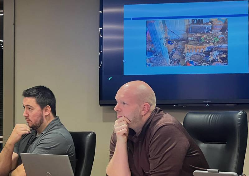 Sterling Aldermen Joe Strabala-Bright (left) and Josh Johnson listen to details about a proposed rental housing ordinance Monday night at Sterling City Hall. Behind them is a photo depicting subpar living conditions that have been found in local rental housing.