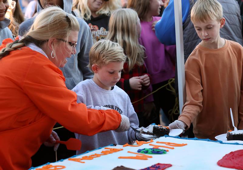 Brandi Voigt, theme director of the Pumpkin Fest Committee, hands cake to Theme Contest honorable mention winners Jaxson Ruby (left) and Leo Berek at the cake cutting ceremony Wednesday, Oct. 23, 2024, on North Maple Street adjacent to the DeKalb County Courthouse during the Sycamore Pumpkin Festival.