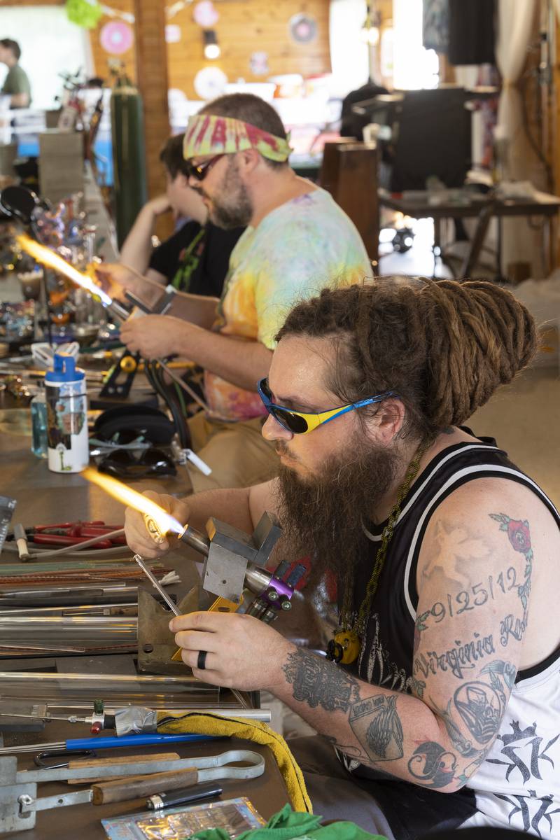 Andrew Kauchak (front) of Machesney Park was one of five glass blowers plying their craft Friday, July 12, 2024 at  Herbal Roots’ Cannafest at Elks Page Park.