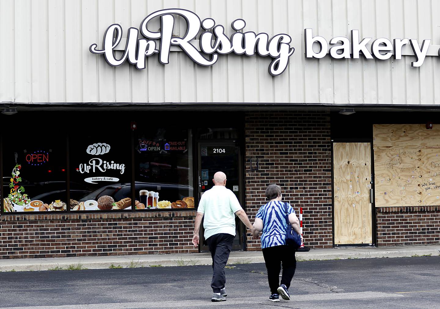 A couple holds hands as they walk into Uprising Bakery & Cafe in Lake in the Hills, Monday, July 26, 2022, after the store reopened Sunday after its front windows were smashed and epithets written on the walls, to long lines and enthusiastic community support. The cafe, which was planning to host an all-ages drag show Saturday night, had experienced backlash over the previous few weeks.