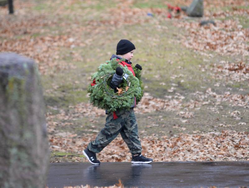 Owen Alrbight, 8, of Mt.Morris carries two wreaths toward veterans' graves during the Wreaths Across America at Daysville Cemetery., east of Oregon, on Saturday, Dec. 16, 2023. Owen was one of several people who helped with the event despite a steady rain and temperatures in the 40s.