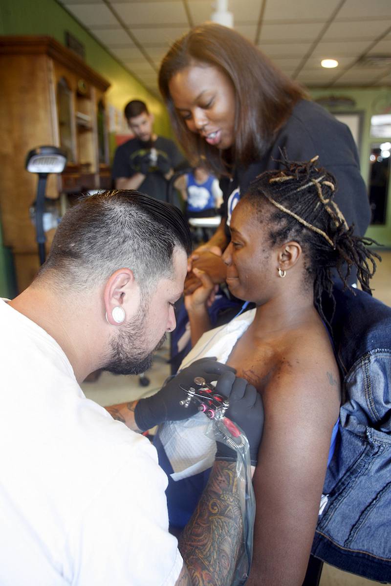 From left, Nicholas Misitano tattoos a feather on the shoulder of Tikila Jackson as Tangela Griffin holds Jackson's hand for moral support.