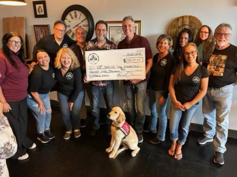 Brats, Bourbon, and Beer board and committee members present a $25,000 check to Jenn Hillery and Tom Bolek of VIP Service Dogs Fund with service dog trainee Walnut.