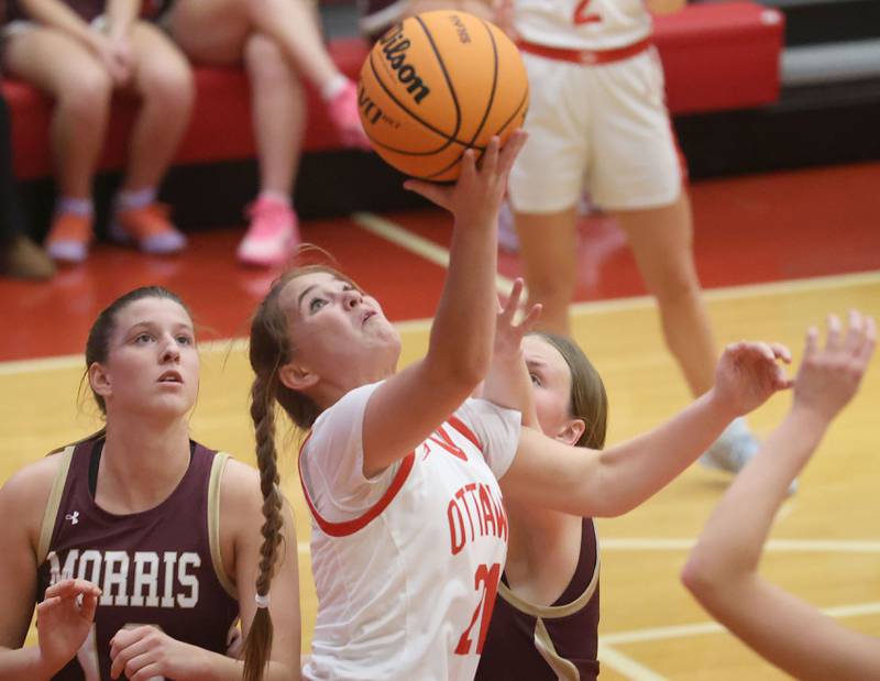 Ottawa's Hailey Thrush (21) tries a reverse layup over Morris defenders Alyssa Jepsen and Brooke Thorson on Tuesday, Dec. 9, 2025, in Kingman Gym at Ottawa High School.