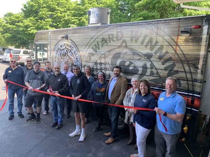 Jim Metallo, owner of Brothers BBQ Truck and Catering Kitchen, cuts the ribbon to celebrate the opening of their new Catering Kitchen.  He is joined by friends, family, and the staff and board of the Cary-Grove Area Chamber of Commerce