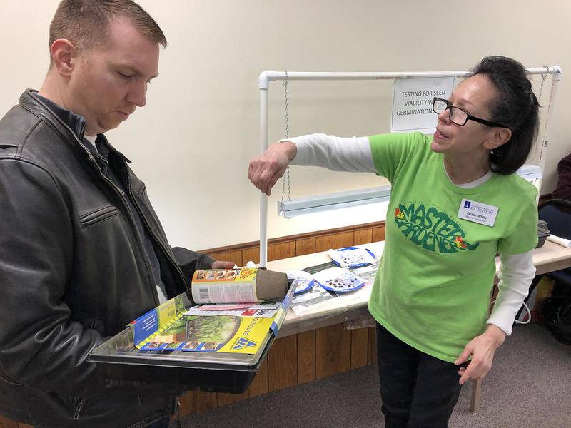 Master Gardener Gloria White (right) shows home gardener Matt Mosteiko how to make a home testing area to test seed viability with germination rates at the Kendall County Master Gardener seed swap Feb. 2.