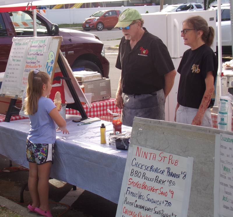 Madelyn Kadelak talks to food vendors from Ninth Street Pub as she enjoys an ice cream cone Sunday, May 28, 2023, during the Music and Art Festival at Pulaski Park in La Salle.