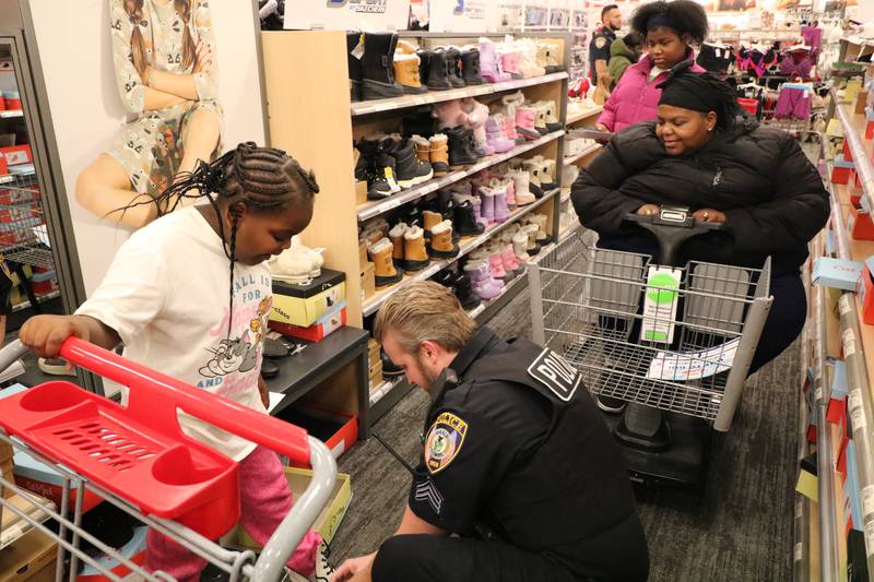 Detective Sgt. Sonny Streit ties the shoelaces for Zinara Winslow, 8, as Ciara Winslow and Sariyae Winslow, 12, look on Sunday, Dec. 15, 2024. Streit accompanied the Winslows during the DeKalb Police Department's Heroes and Helpers event at DeKalb Target.