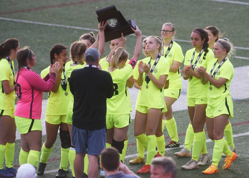 Richmond-Burton players surround the second-place trophy after losing to Quincy Notre Dame in Saturday’s IHSA Class 1A state girls soccer championship game at North Central College in Naperville.