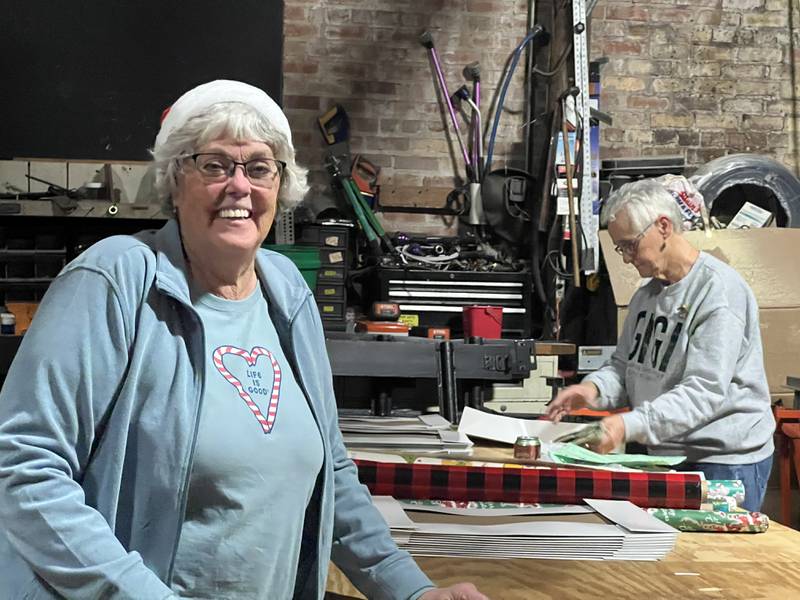 President of the DeKalb and Sycamore Goodfellows, Sandy Lancaster (left) wears a Santa hat while Christel Springmire begins wrapping gifts at the Goodfellows gift wrapping party inside Blumen Gardens on Dec. 13, 2023.