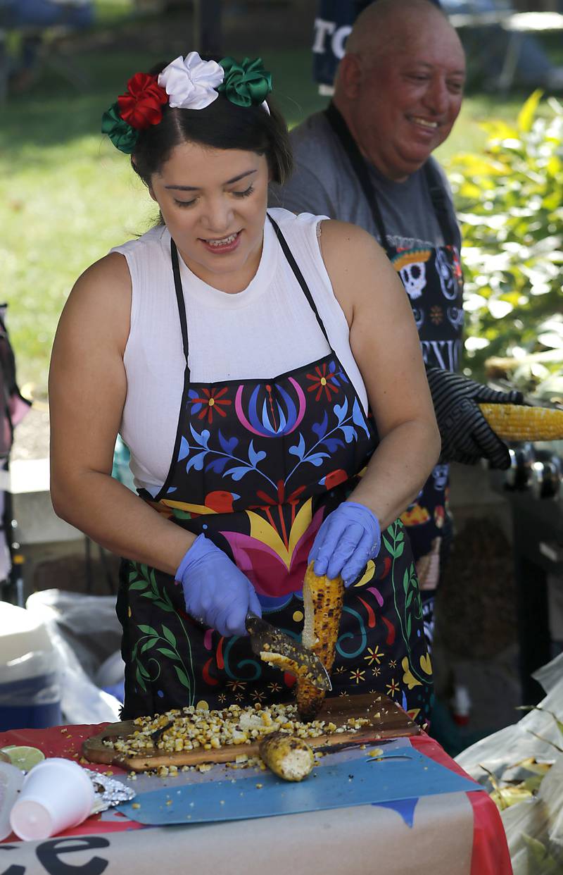 Alondra Diaz cuts corn off the cob as she make Mexican roasted corn at the Save Me a Piece booth  on Sunday, Sept. 14, 2025, during the annual Hispanic Connections Mexican Independence Day Celebration in the Historic Woodstock Square. The celebration featured music, food and culture.