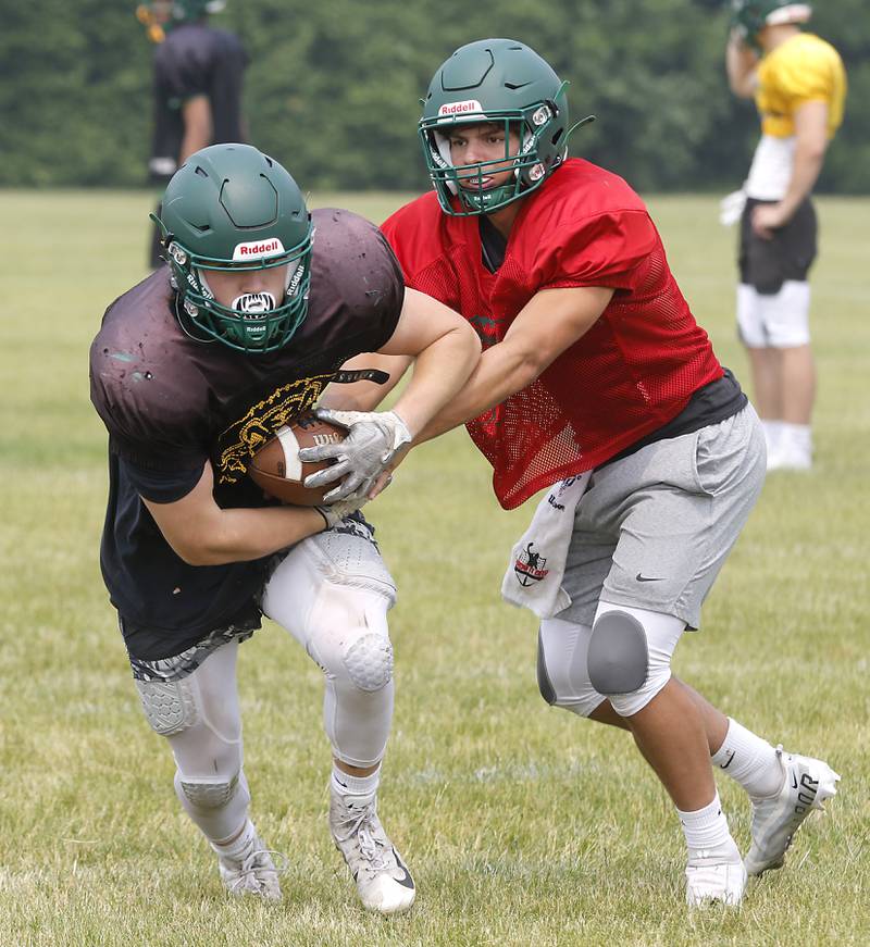 Crystal Lake South quarterback Caden Casimino hands the ball off to Jake Christensen during football practice Tuesday, June 27, 2022, at Crystal Lake South High School.