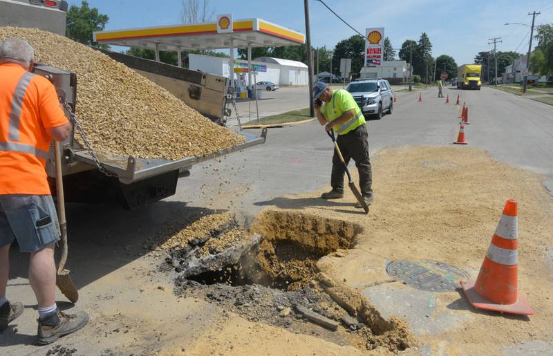 Travis Coil of Martin & Co. (right) and Polo Public Works Director Kendall Kyker watch as chip gravel is dumped into the large sink hole that developed in the east lane of Illinois 26 in Polo late Friday afternoon. Underneat the concrete and pavement, the hole measured 10' long, 7' wide and about 10' deep. It was filled with the gravel as a temporary fix until crews can repair the storm sewer leak.