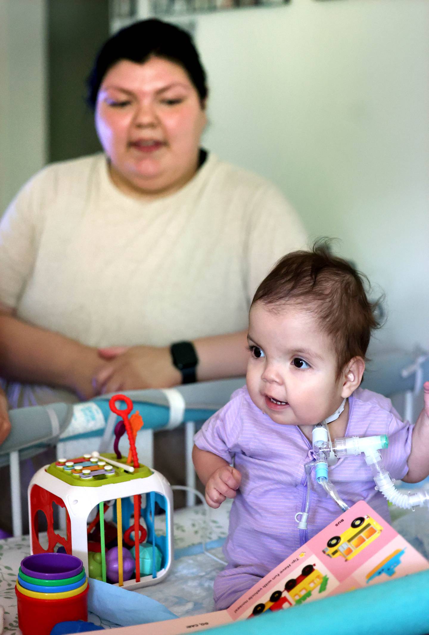 Marely Chavarria Santos, 1, plays in her crib as her mom Kassandra Santos looks on Monday, June 30, 2025, at their home in DeKalb. Marely was born with a myriad of health issues that require around-the-clock care and recently received a heart transplant.