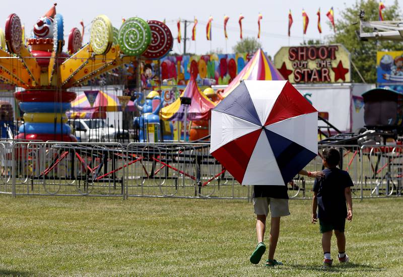 Two boys use an umbrella for shade as they walk the midway to see what rides they would like to ride during the opening day of the McHenry County Fair on Tuesday, July 29, 2025. The fair runs through Sunday at the fairgrounds in Woodstock.
