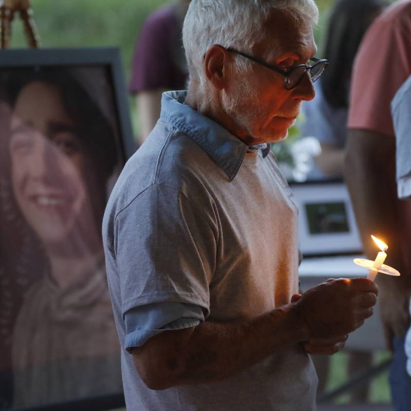 Peter Passuntino holds a candle as “Amazing Grace is sang during a candlelight celebration for his grandson, Riely Teuerle, pictured behind him, on Thursday, August 11, 2022, at Towne Park, 100 Jefferson Street in Algonquin. Teuerle was killed in a car crash in Lake in the Hills on Tuesday. Over 100 family members and friends gathered at the park to remember and celebrate Teuerle’s life.