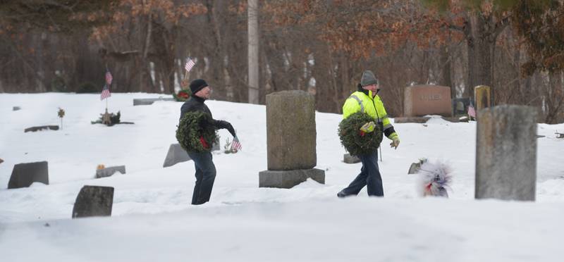 Two volunteers trudge through the snow to lay wreaths on veteran graves at the Daysville Cemetery, southeast of Oregon, during the Wreaths Across America program on Saturday, Dec. 13, 2025.