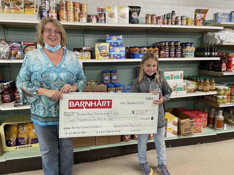 On behalf of Barnhart Crane and Rigging Co. in Ladd, Marley Pelka presents Mendota Area Christian Food Pantry with a Barnhart Community Care Grant of $2,000.