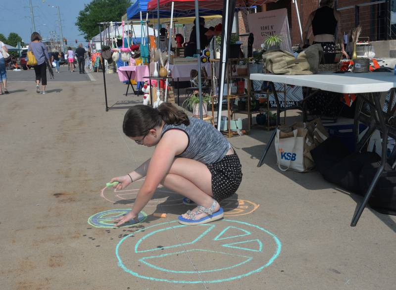 Noah Stach, 11, of Dixon draws peace symbols no the sidewalk in front the Peace & Art Projects booth at the Dixon City market on Wednesday.